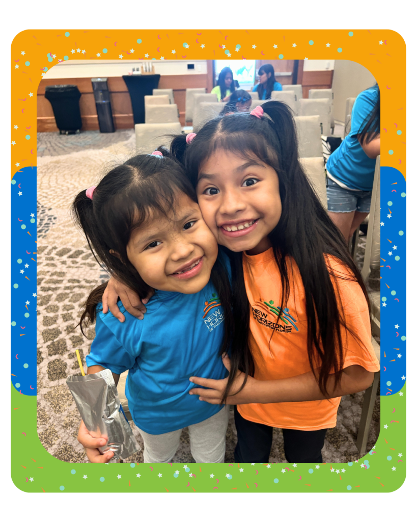 Two elementary school students in New Horizons of SWFL t-shirts smile with their arms around each other.